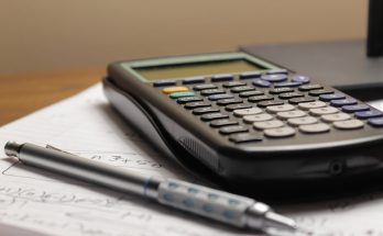 A calculator and pen lying on a sheet of paper with mathematical notes.