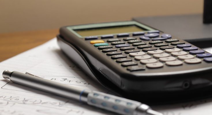 A calculator and pen lying on a sheet of paper with mathematical notes.