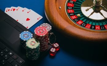Close-up view of poker chips, playing cards, a roulette wheel, and a laptop on a blue table