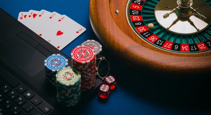 Close-up view of poker chips, playing cards, a roulette wheel, and a laptop on a blue table